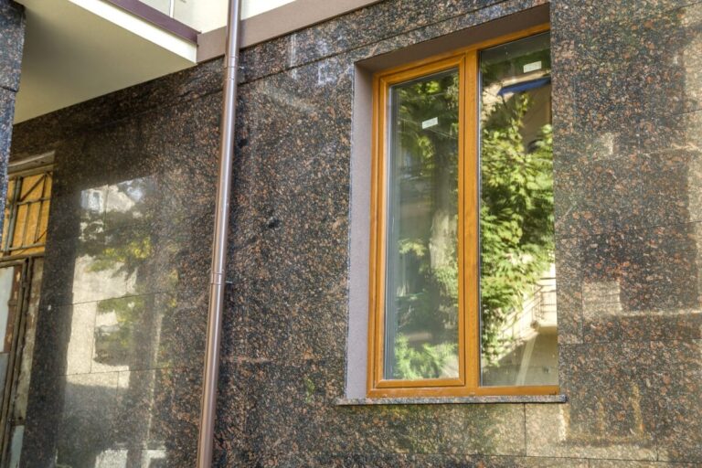 Okno budynku z drewnianą ramą i parapetami granitowymi.