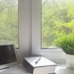 Tablet, notes i roślina stoją na parapetach z konglomeratu z widokiem na zielony las.