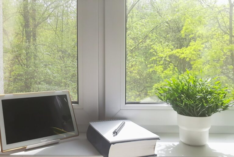 Tablet, notes i roślina stoją na parapetach z konglomeratu z widokiem na zielony las.