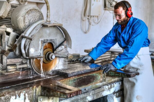 Mężczyzna pracujący przy maszynie do cięcia kamienia świadczy usługi kamieniarskie.
