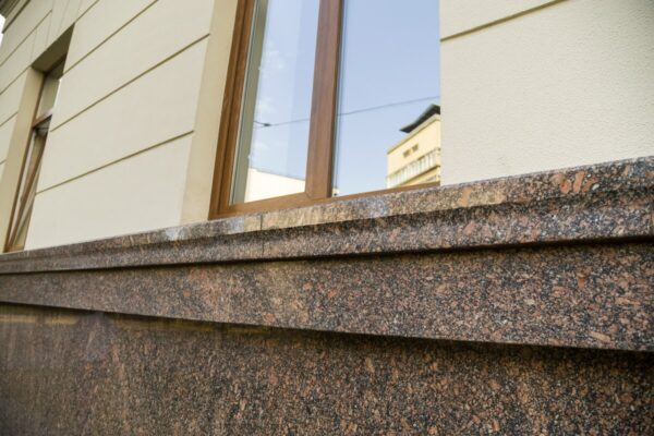 Okna z eleganckimi parapetami marmurowymi na tle jasnej elewacji budynku.